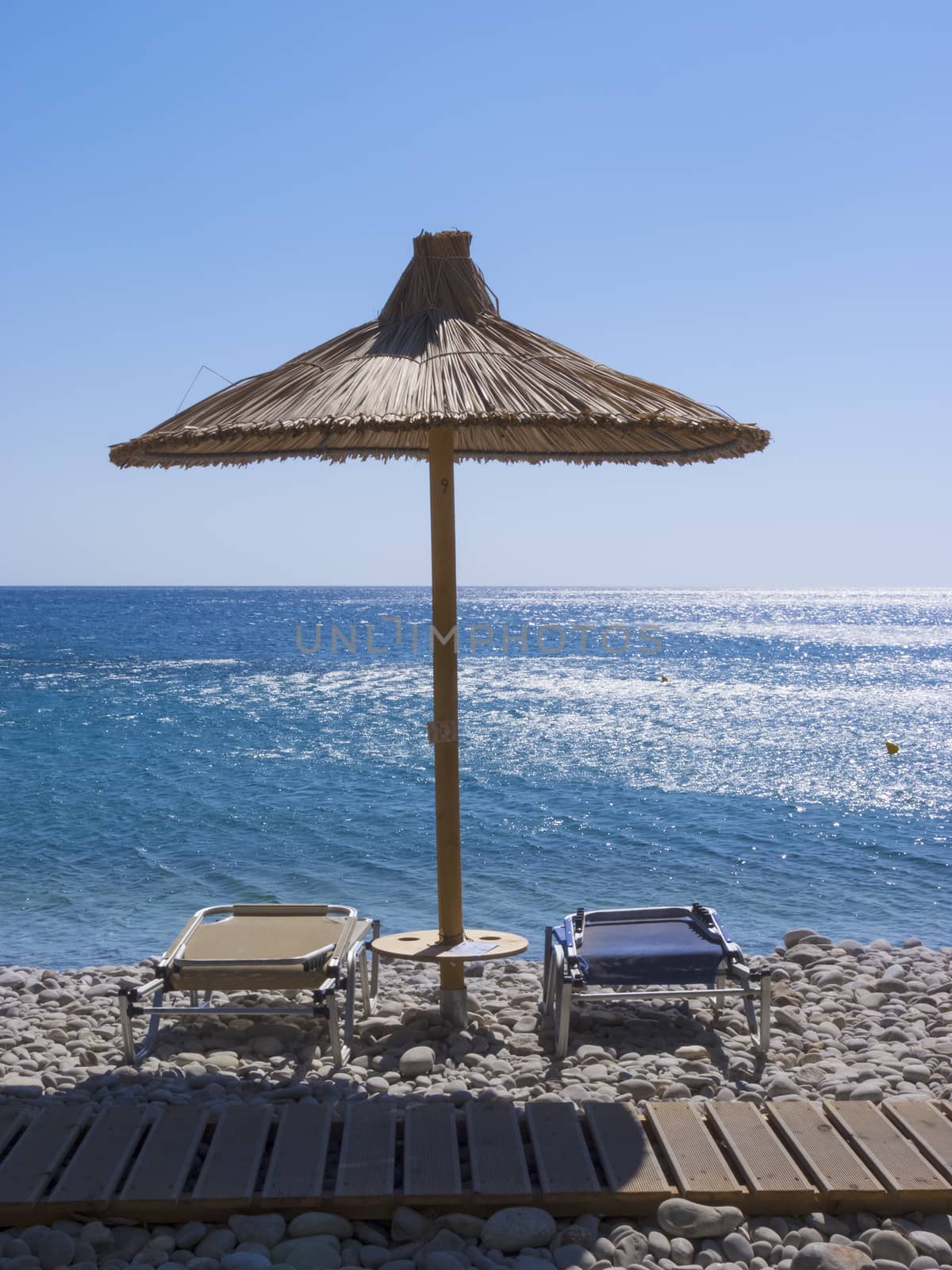 Reed umbrella and two deck chairs on the sea beach