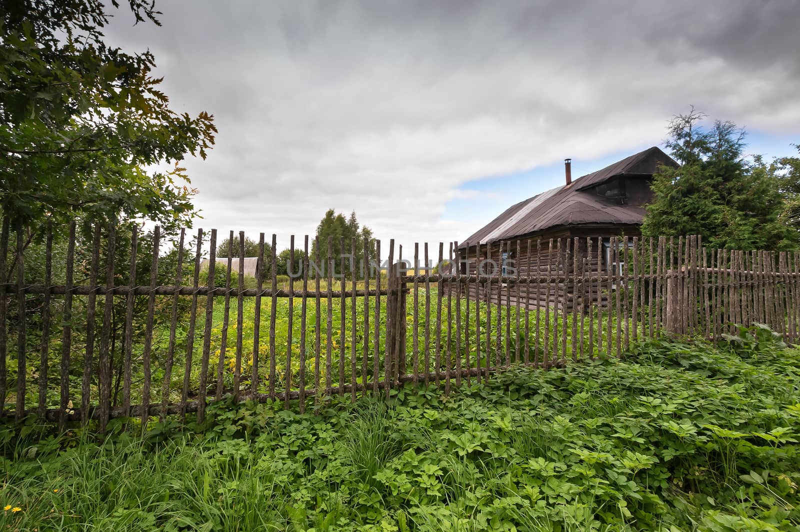 Old village house behind a wooden fence. The grassy area.