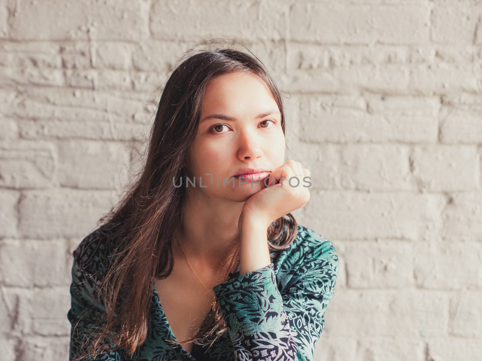 Stern and serious looking young brunette beauty. Closeup portrait of serious young woman with sensual look at camera. Girl rests her chin on hand and serious looking at camera.