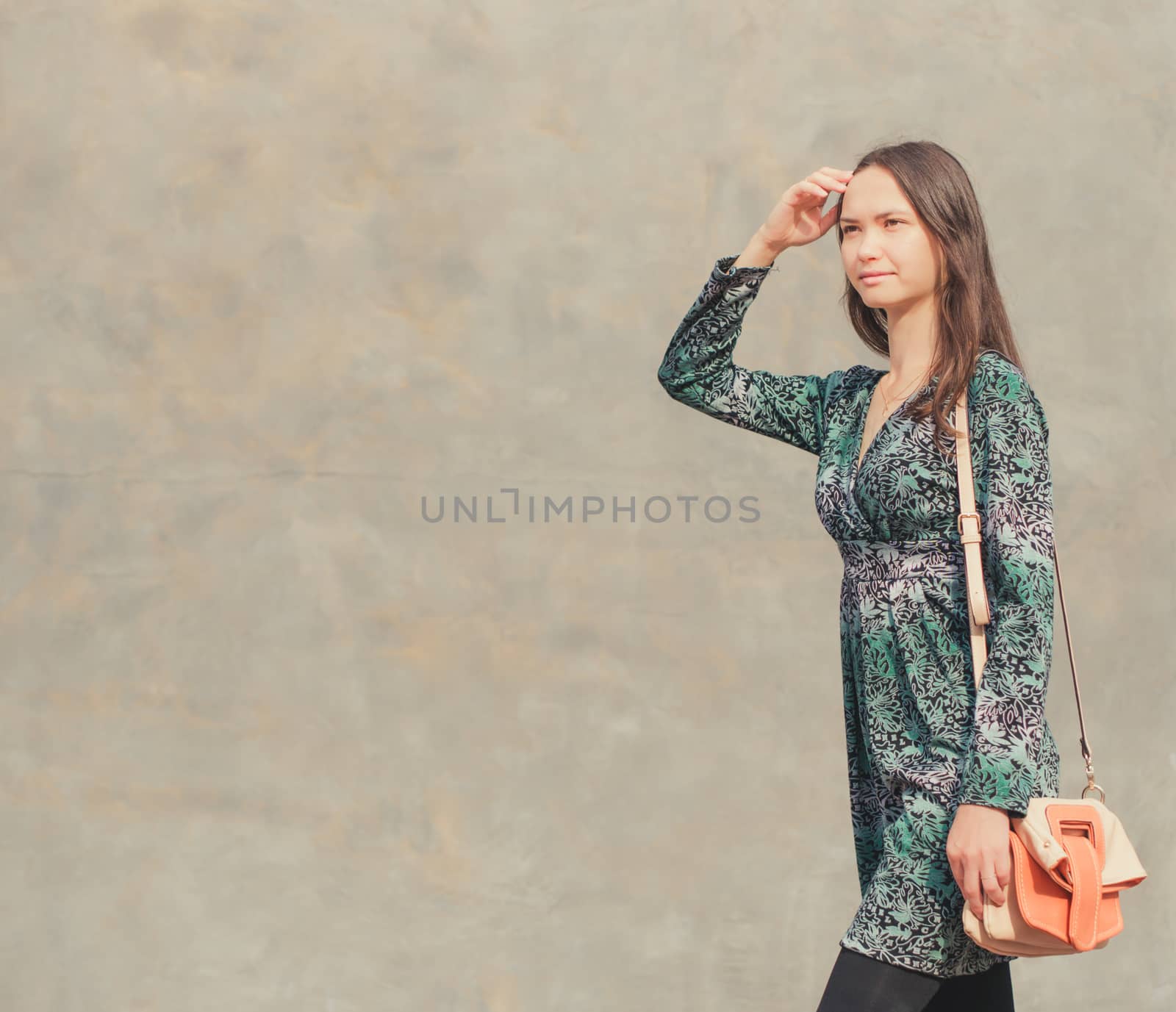 Side view of caucasian woman walking on city street in front of gray wall. Copy space