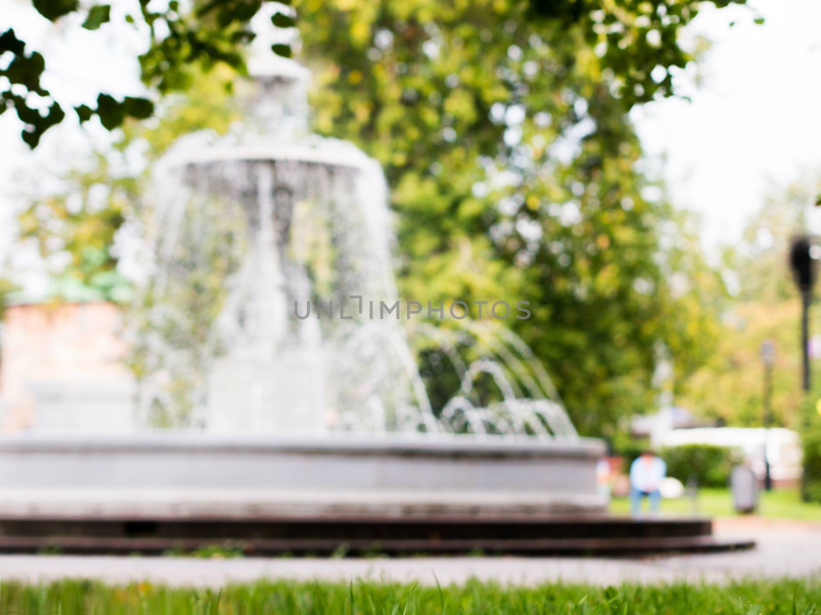 blurred of fountain and green foliage, out of focus image. Fountain and green trees as background