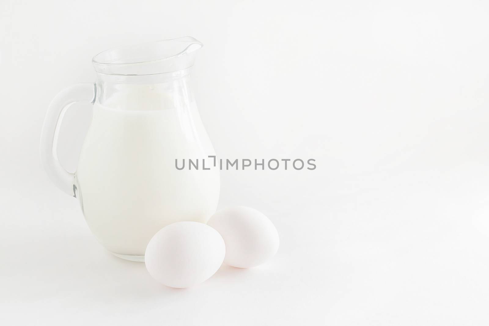 jug with milk and two eggs on white background.