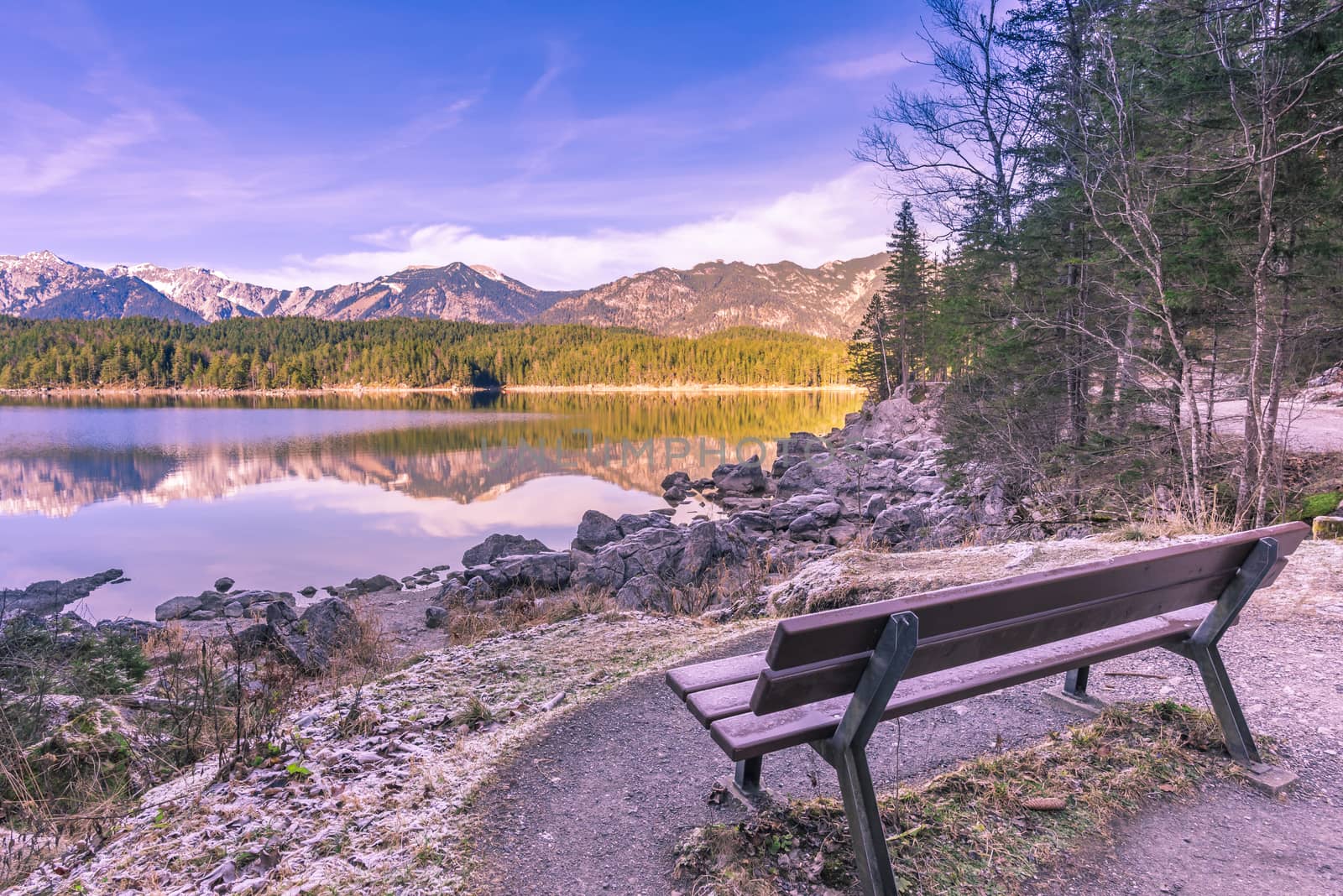 Winter image with a bench located on the shore of the Eibsee lake, from Grainau, Germany. Reflected in its water are the Bavarian Alps mountains.