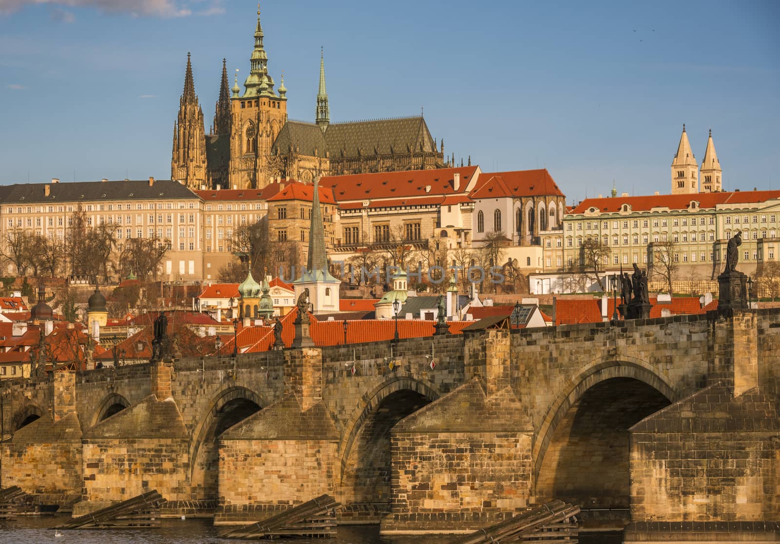 Close up with the stone built Charles Bridge and the St. Vilus Cathedral, surrounded by other historical buildings, in the background.