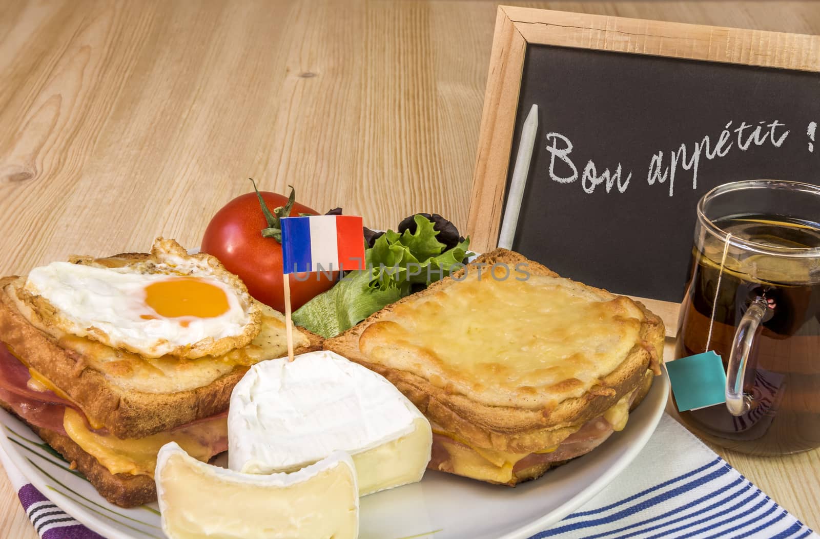 Traditional french sandwiches, croque madame and croque monsieur, fine cheese and fresh salad, placed on table and near it a chalkboard with the message of bon appetit.