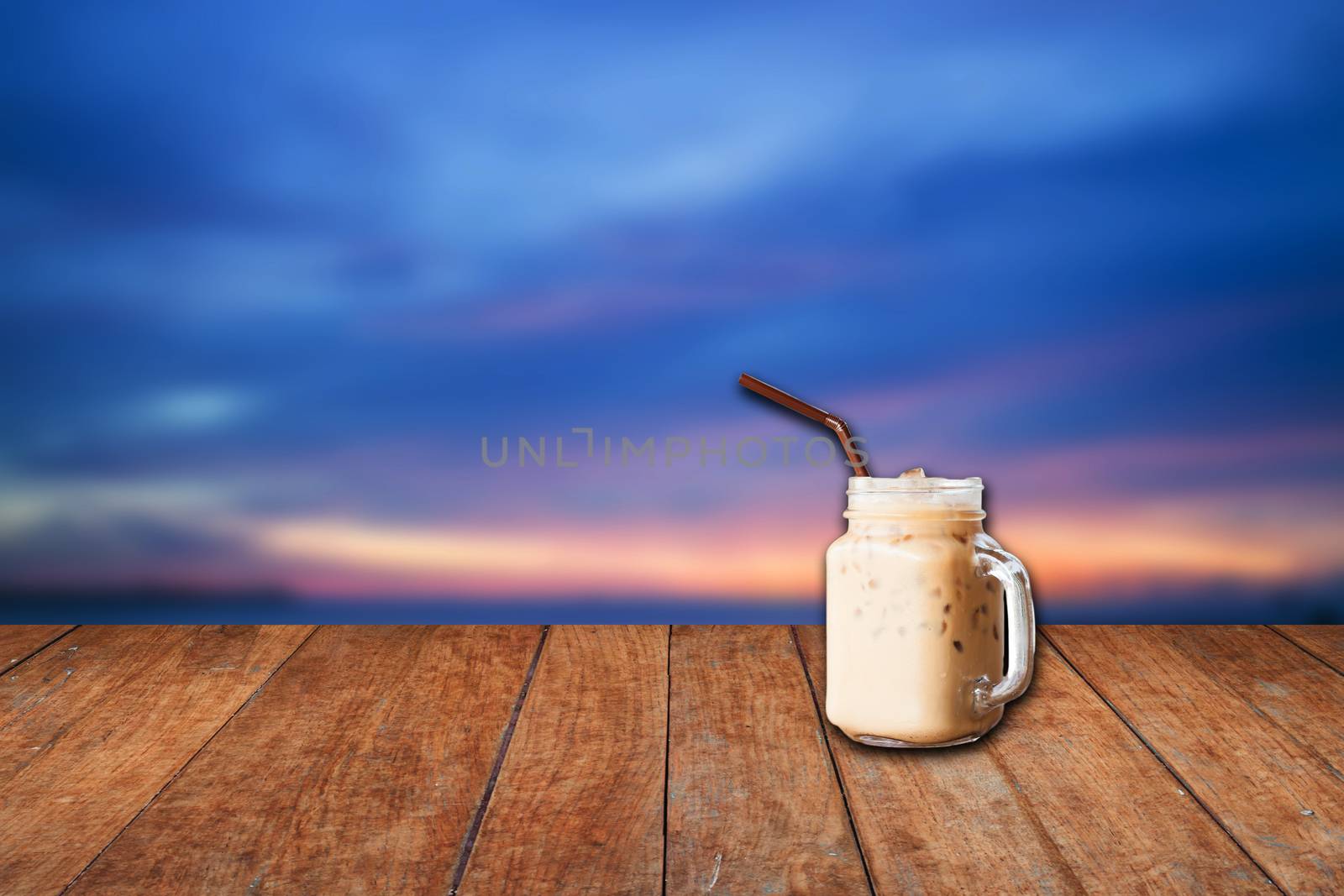 Iced coffee cup with blue sunset sky and wood floor background