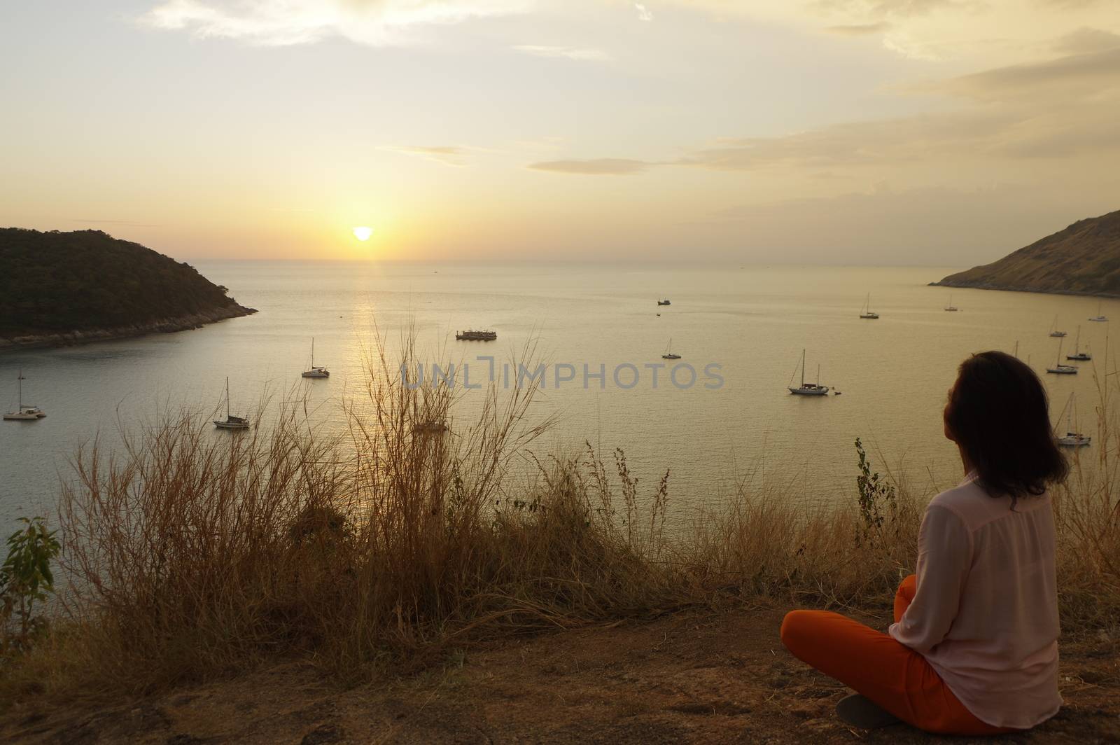 Young girl sitting in yoga lotus meditation position front to seaside on the rocks an watching the sun goes down in a golden hour. sunset over sea. by evolutionnow