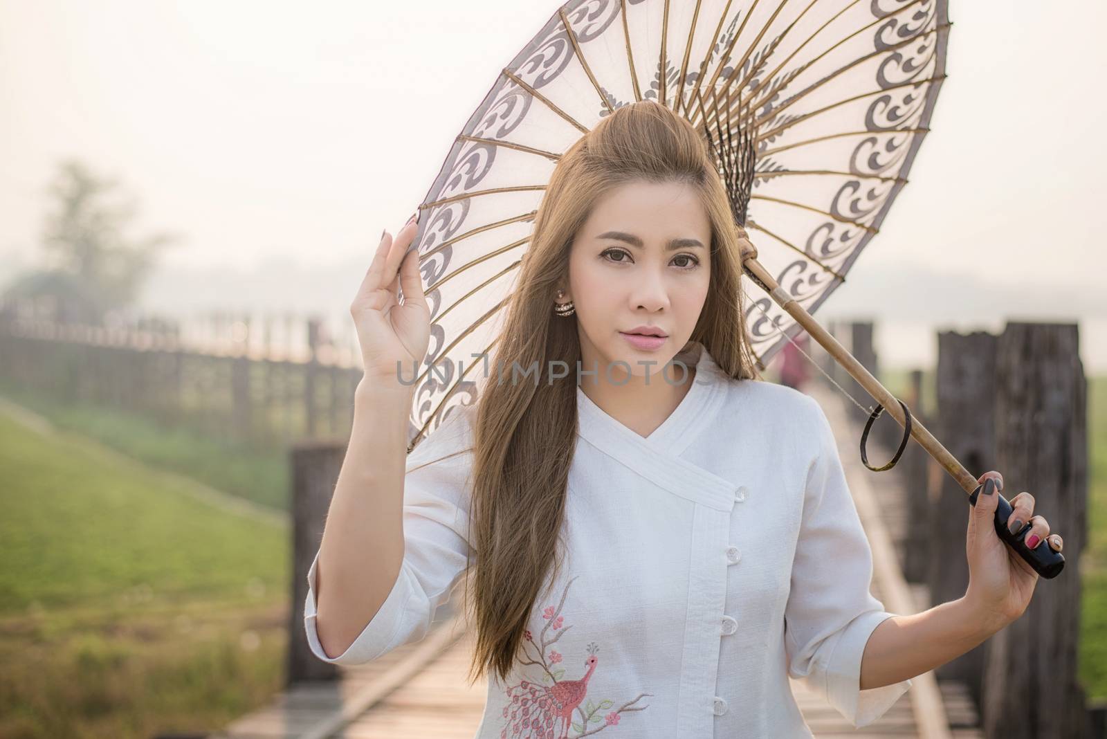 The beautiful Burmese woman in Myanmar traditional costume,with umbrella walking on Ubein bridge, Mandalay Myanmar 