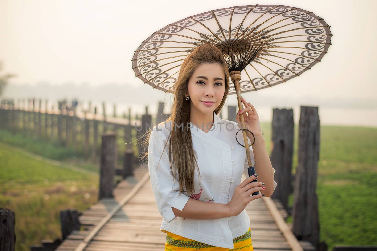 The beautiful Burmese woman in Myanmar traditional costume,with umbrella walking on Ubein bridge, Mandalay Myanmar 