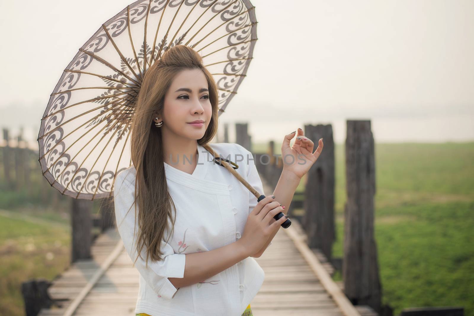 The beautiful Burmese woman in Myanmar traditional costume,with umbrella walking on Ubein bridge, Mandalay Myanmar 