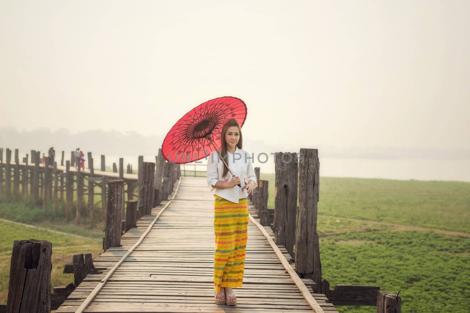 The beautiful Burmese woman in Myanmar traditional costume,with red umbrella walking on Ubein bridge, Mandalay Myanmar 
