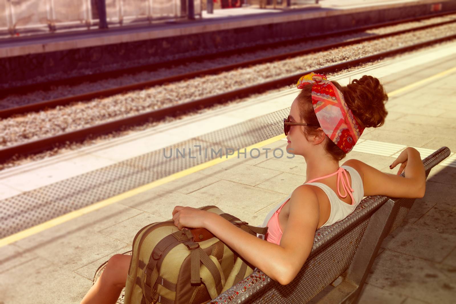 Young sexy woman backpacker sitting on bench on railway station. Travel concept.