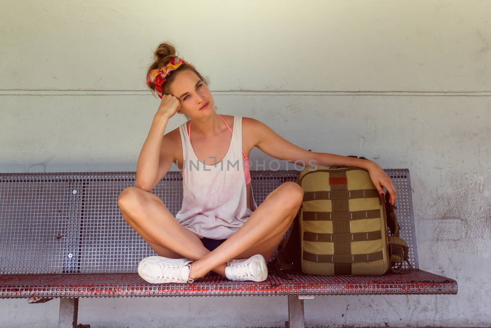 Young sexy woman backpacker sitting on bench on railway station.Travel concept.