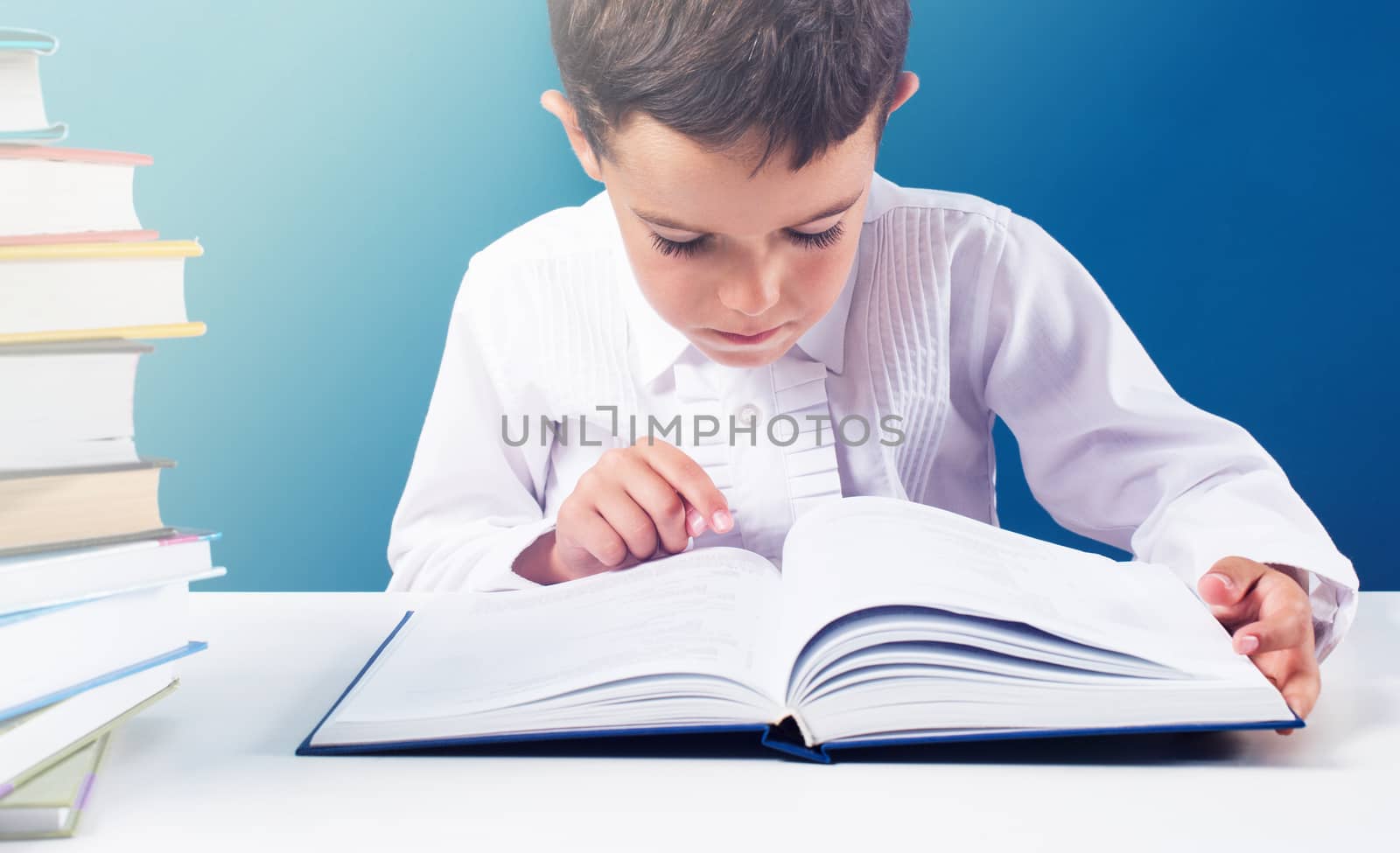 Сute boy reading book at the table, blue background