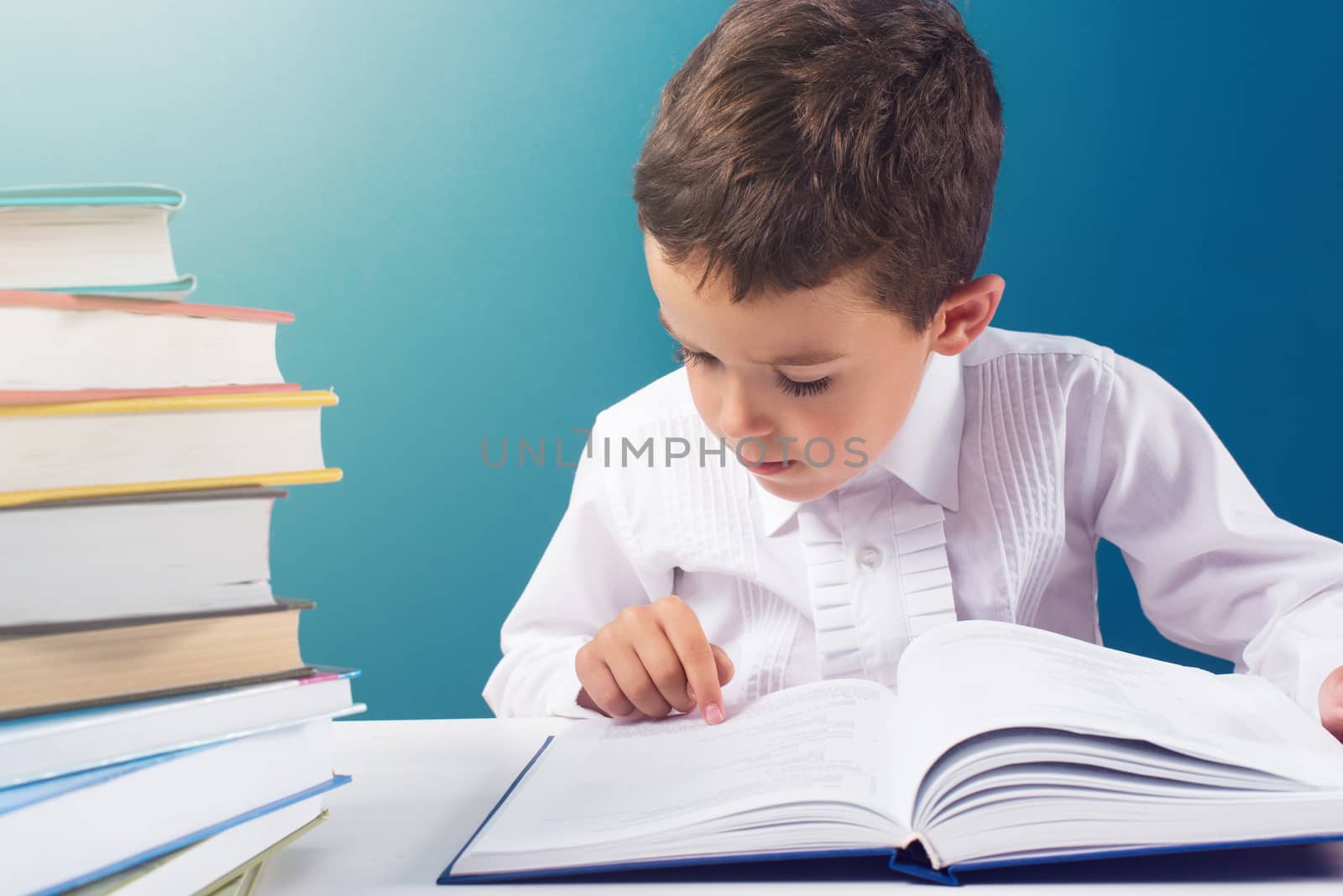 Сute boy reading book at the table, blue background