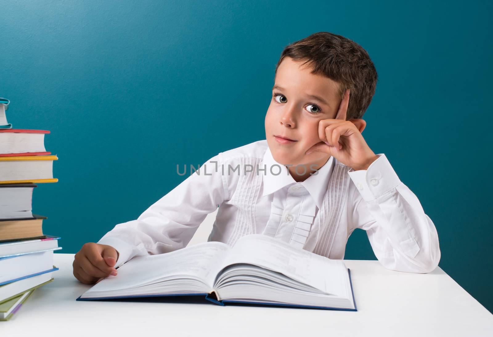 Сute boy with  book at the table, blue background