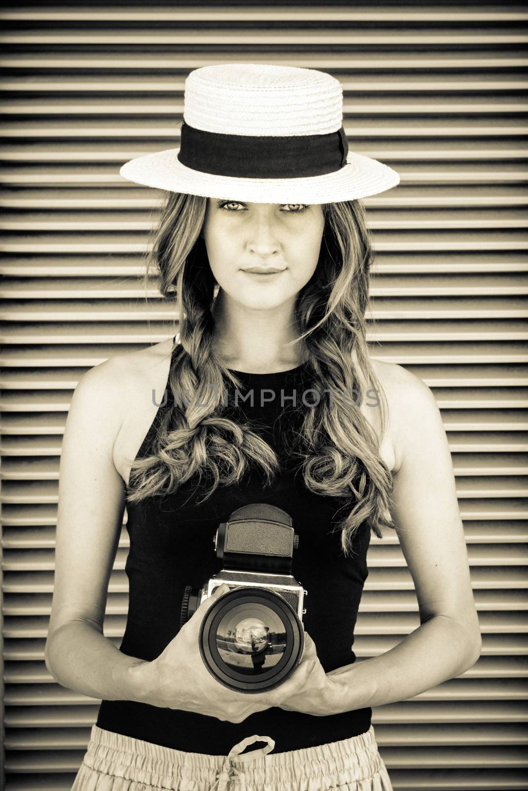 Attractive sexy woman in hat with big professional photo camera against tripped wall