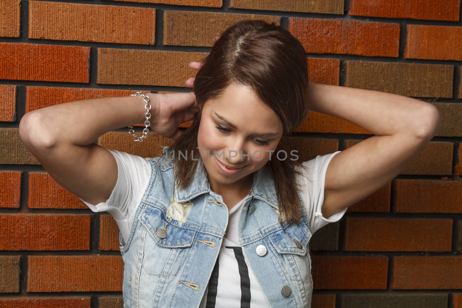 young woman against brick wall, tying her hair up