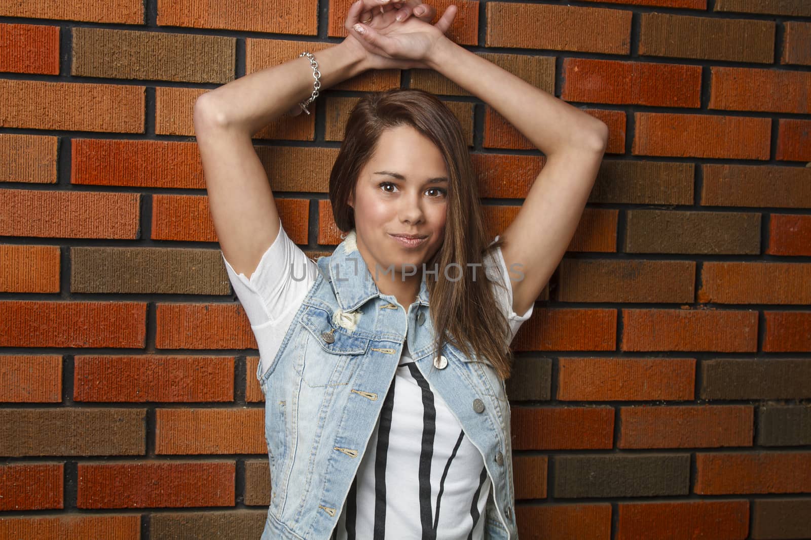young woman relaxing against brick wall with her arms up