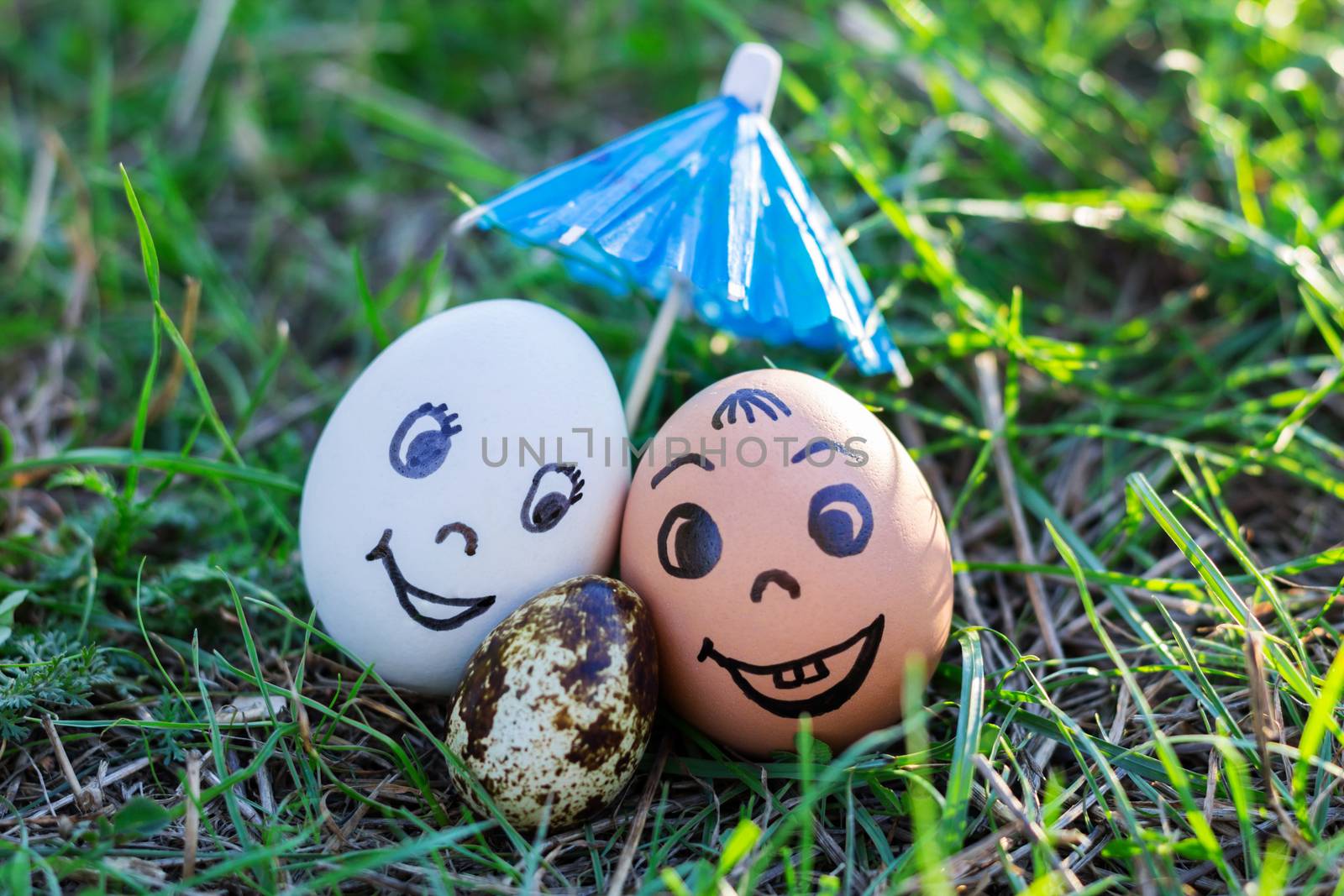 Funny eggs imitating happy smiling mixed couple white and colored parents with versicolored baby under umbrella