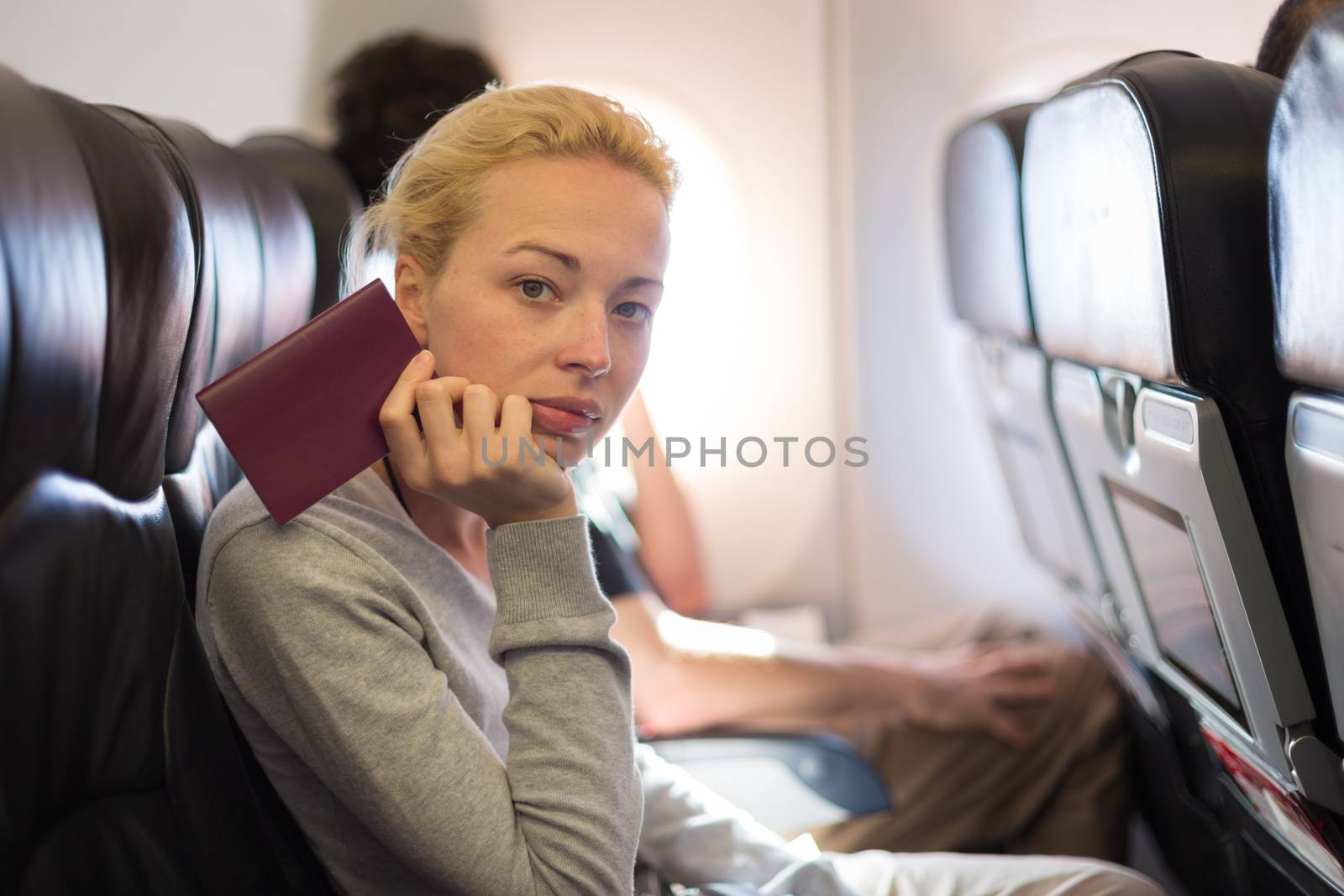 Woman flying by commercial airplane, sitting on her seat, holding passport in her hand, waiting to arrive at immigration point.