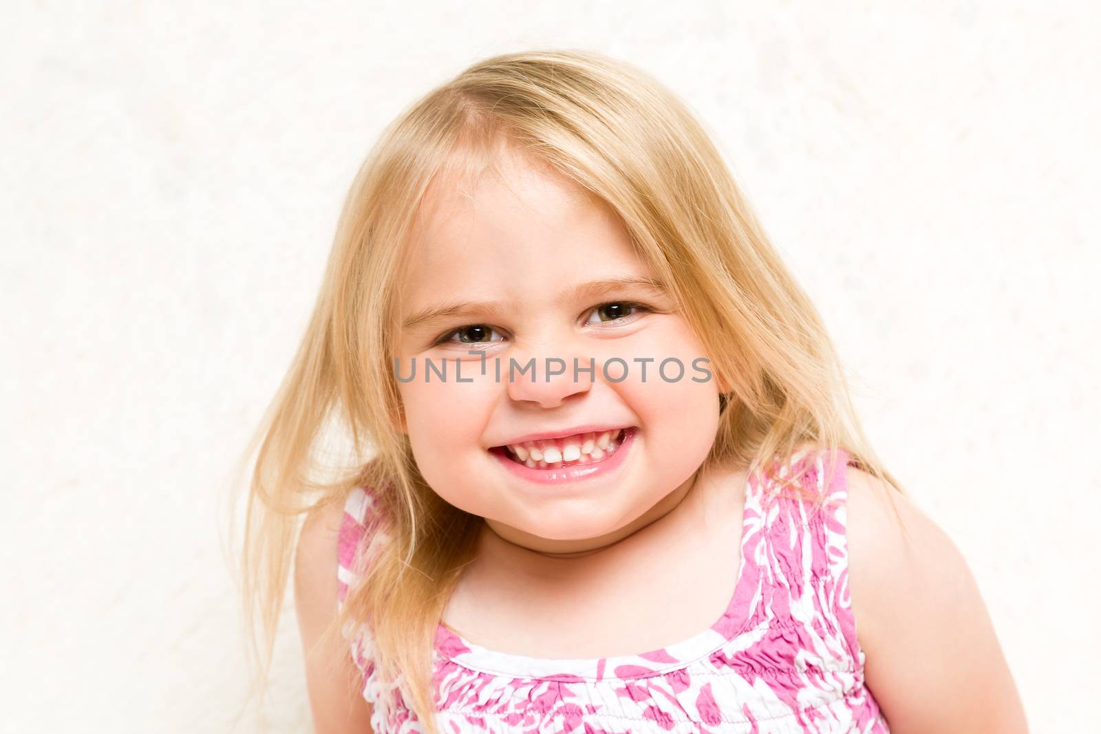 Closeup Portrait of Beautiful Toddler Girl Grinning Cheekily on Neutral Background