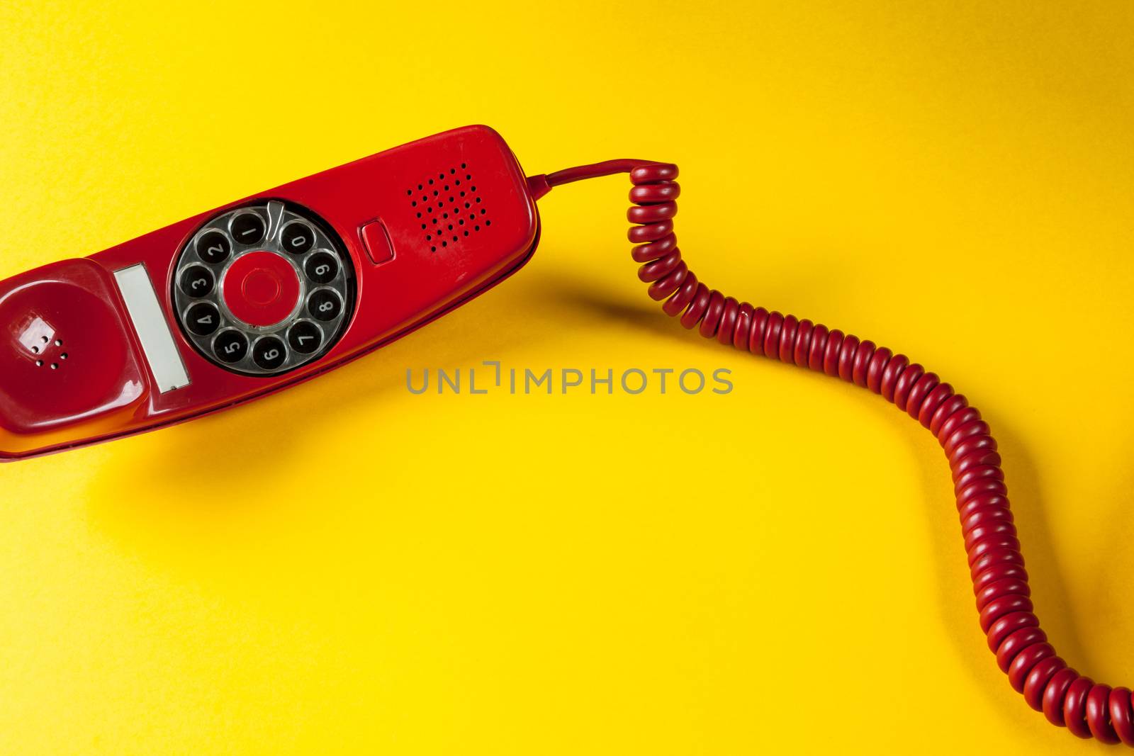 Old red phone off the hook on yellow background