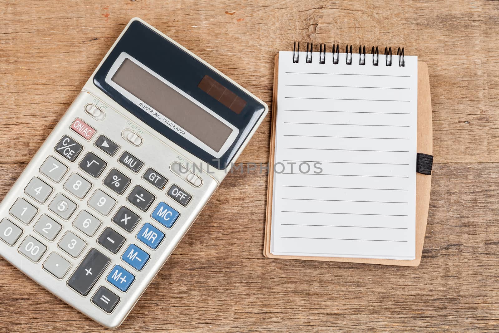 notebook showing empty page  and calculator on wooden desk