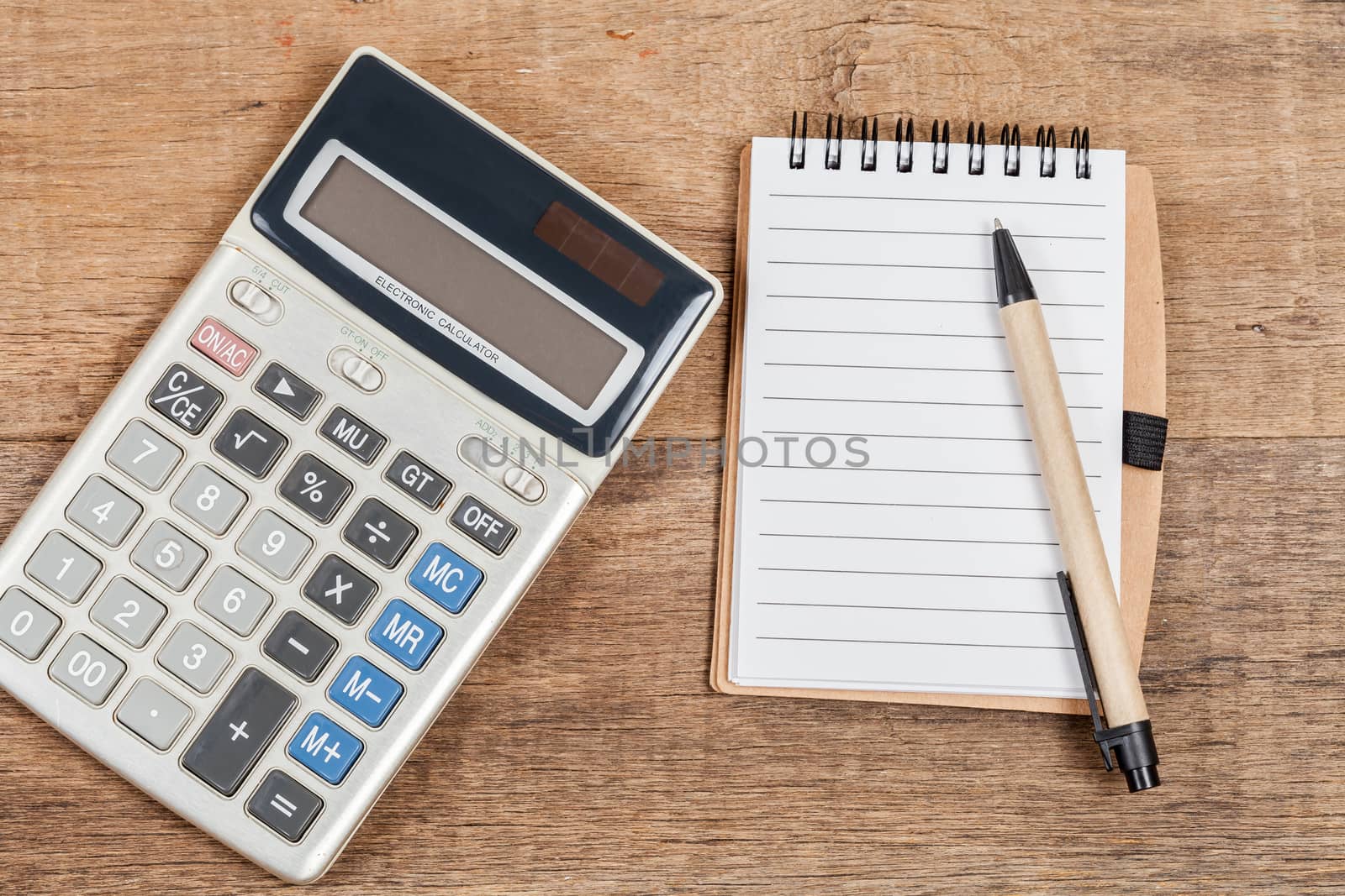 notebook showing empty page  and calculator on wooden desk