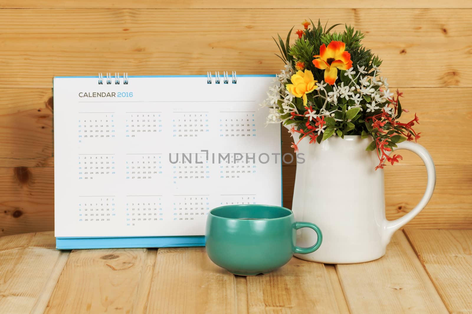 Blank calendar with cup and vase on wood table with yellow light tone
