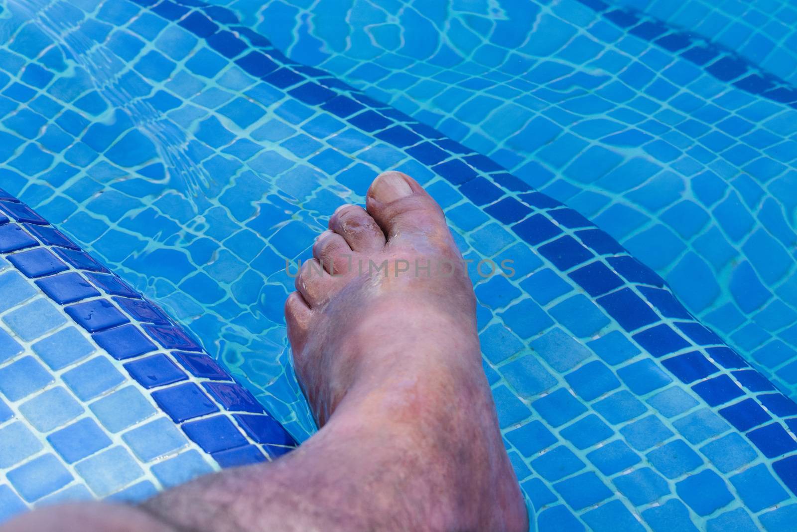 Men feet in a beautiful swimming pool with blue tiles.