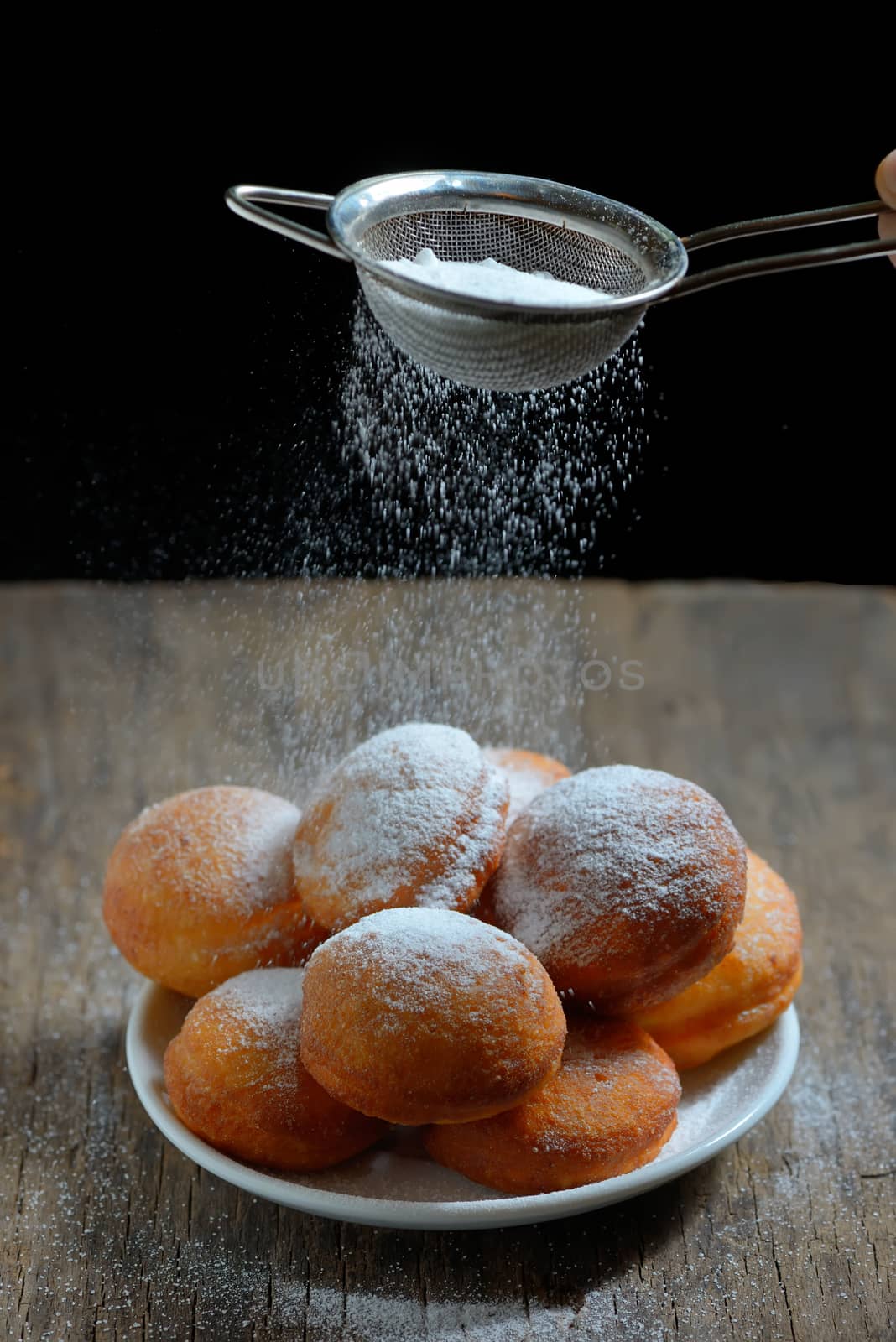 pours sugar with strainer over donuts 