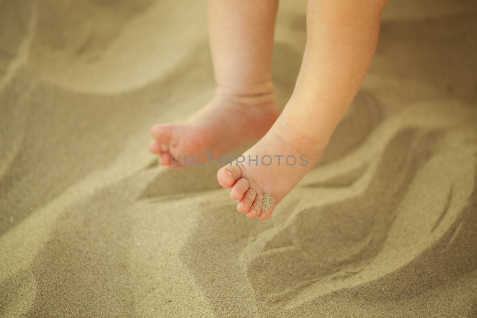 Newborn baby feet playing in the sand in summertime