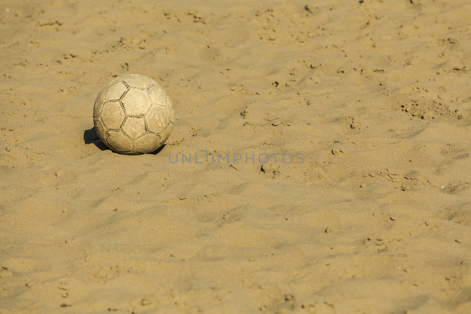 Ruined soccer ball on beach sand on summertime