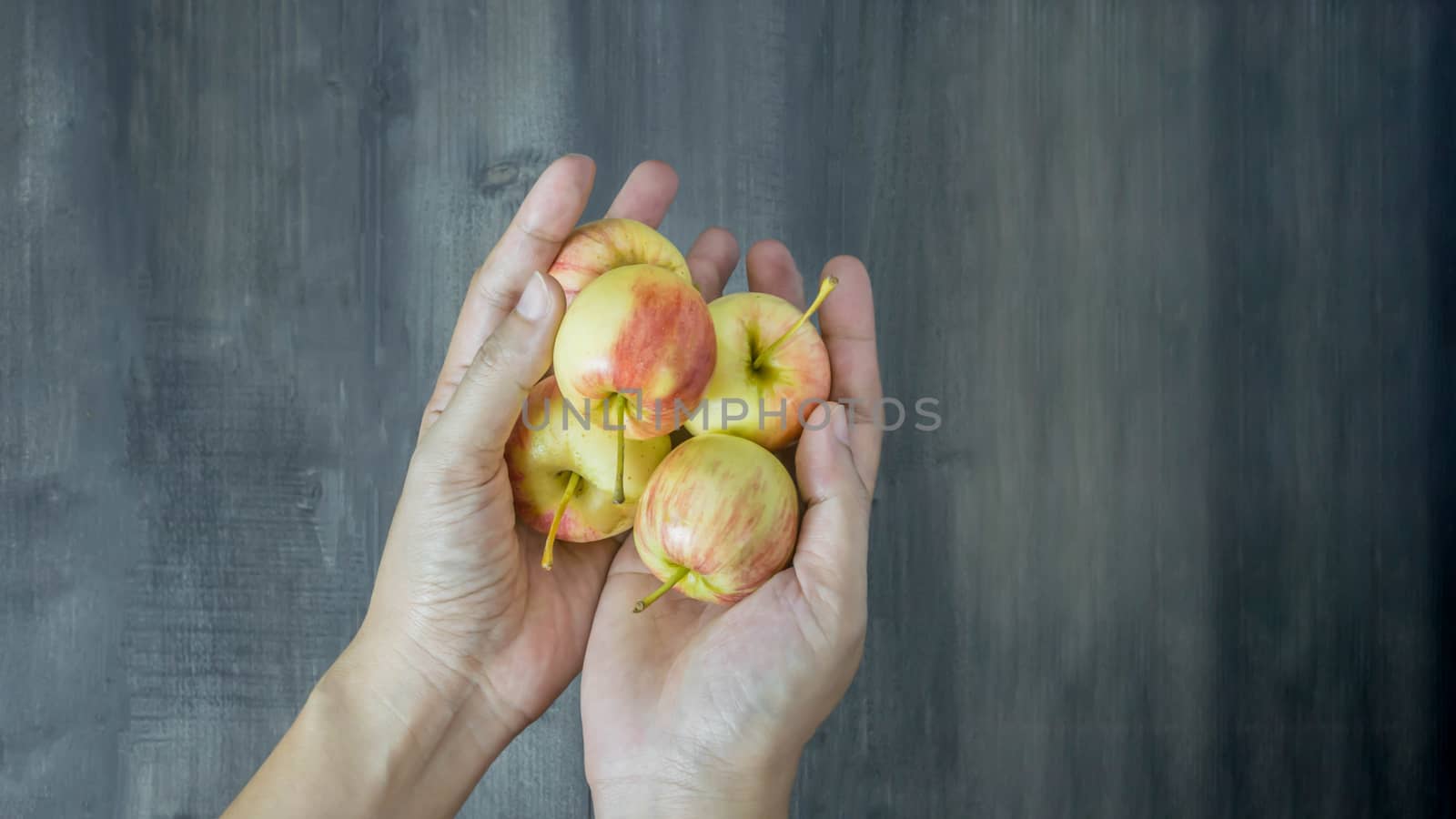human hand holding red and yellow apple  on wooden background , Top view