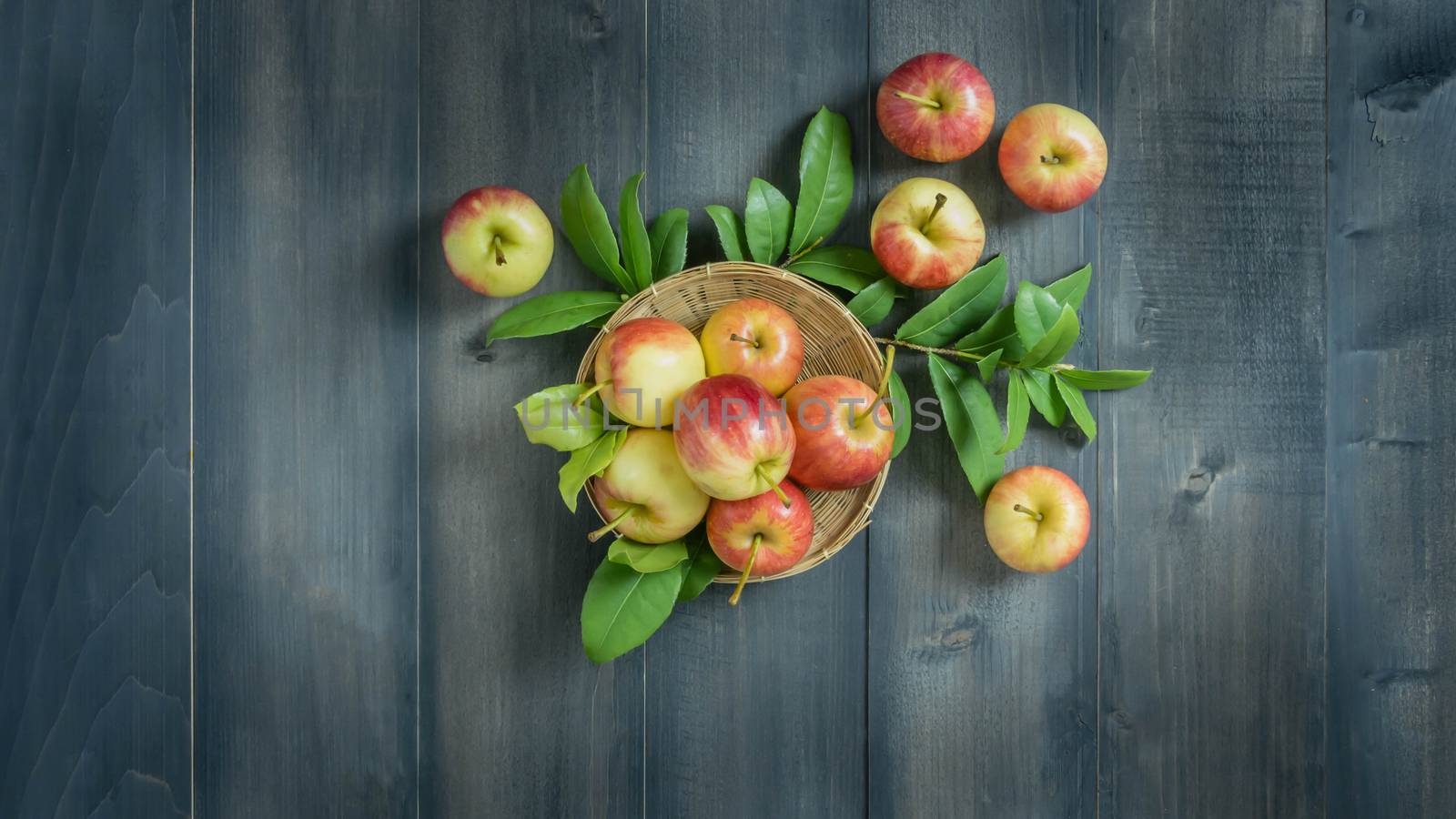 Top view red and yellow apple with leaves and  bamboo basket on wooden background with free space for text