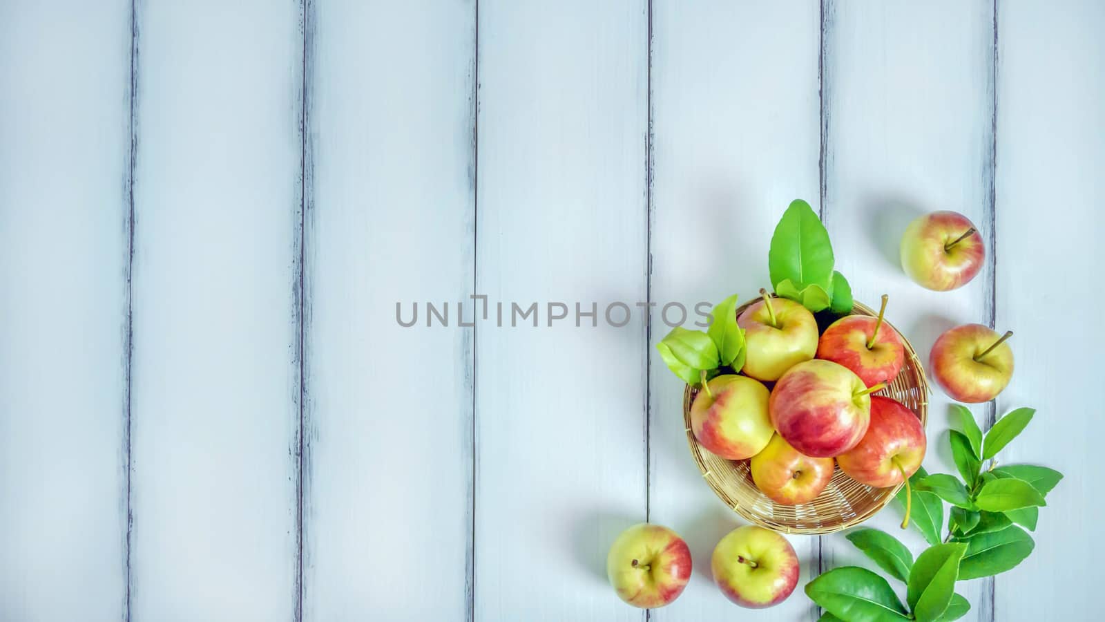 Top view red and yellow apple with leaves and  bamboo basket on  white wooden background with free space for text