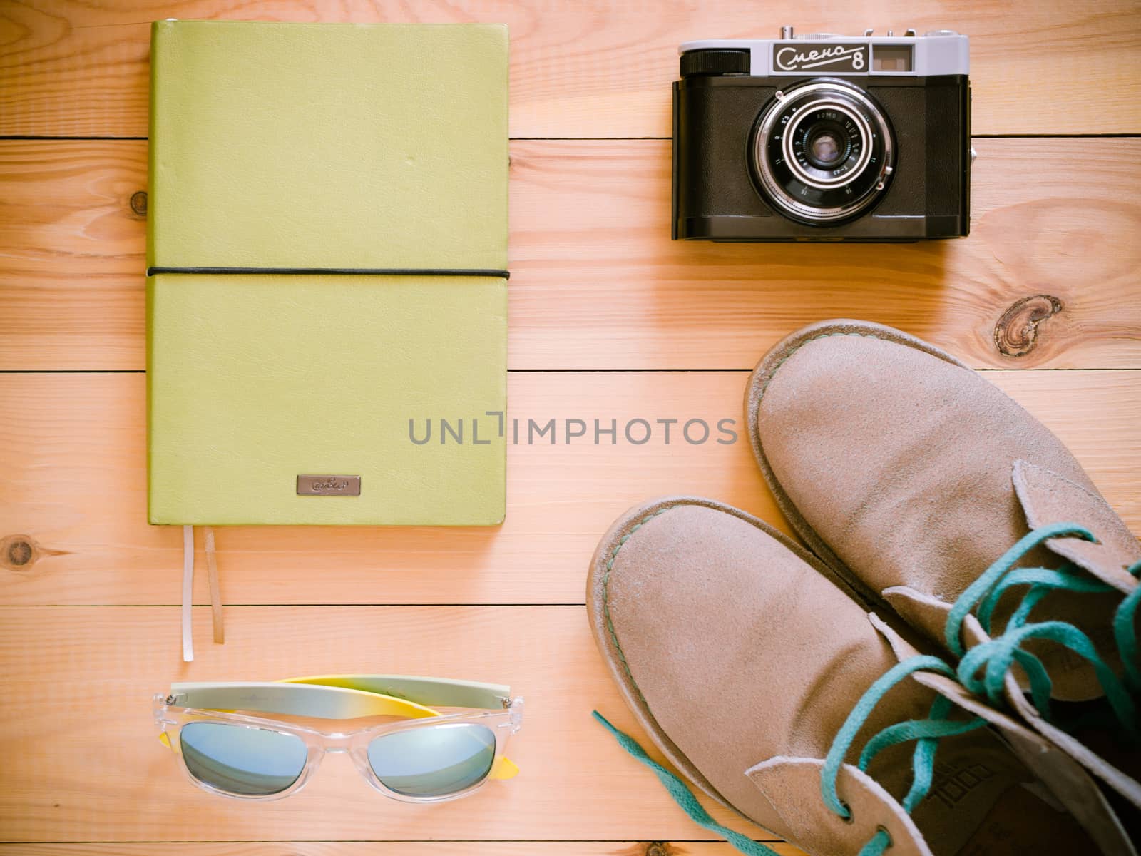 Set of travel and resort stuff. Old 35 mm camera, note book, sunglasses and desert boots on wooden table. Top view, flat lay. Toned image