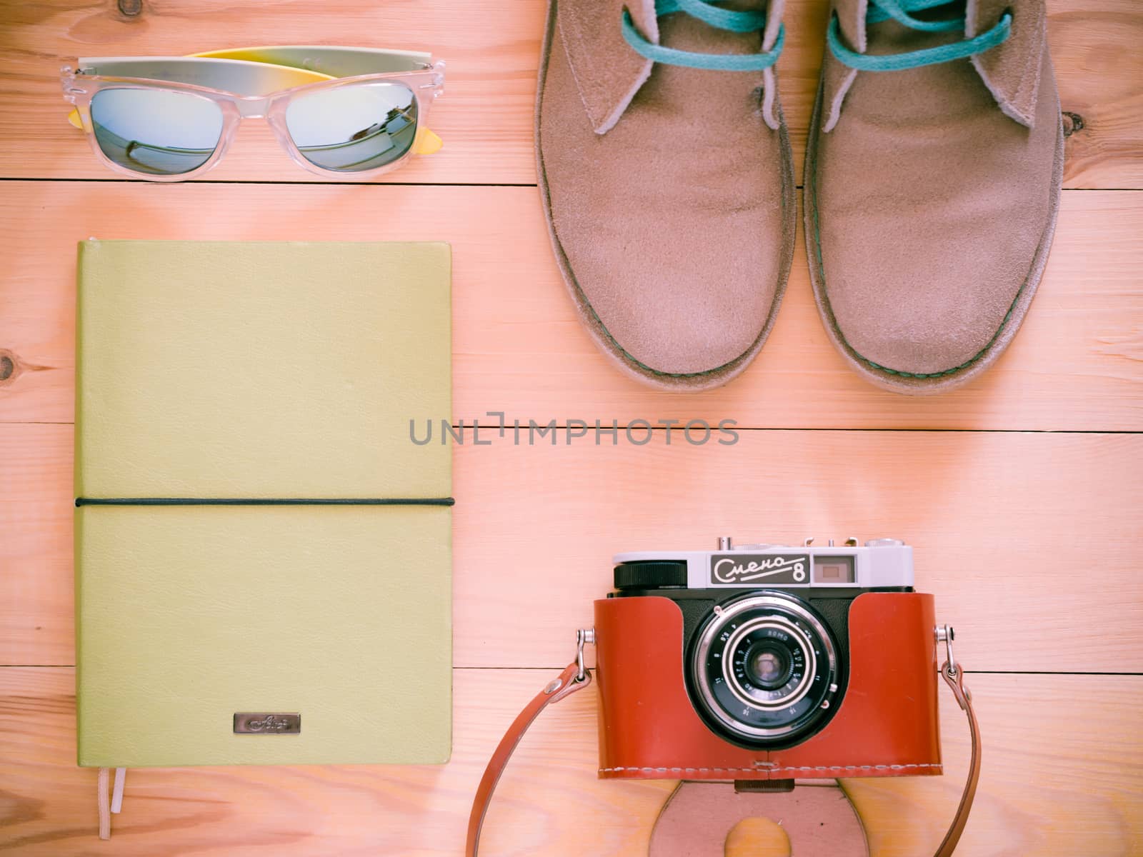 Set of travel and resort stuff. Old 35 mm camera, note book, sunglasses and desert boots on wooden table. Top view, flat lay. Toned image