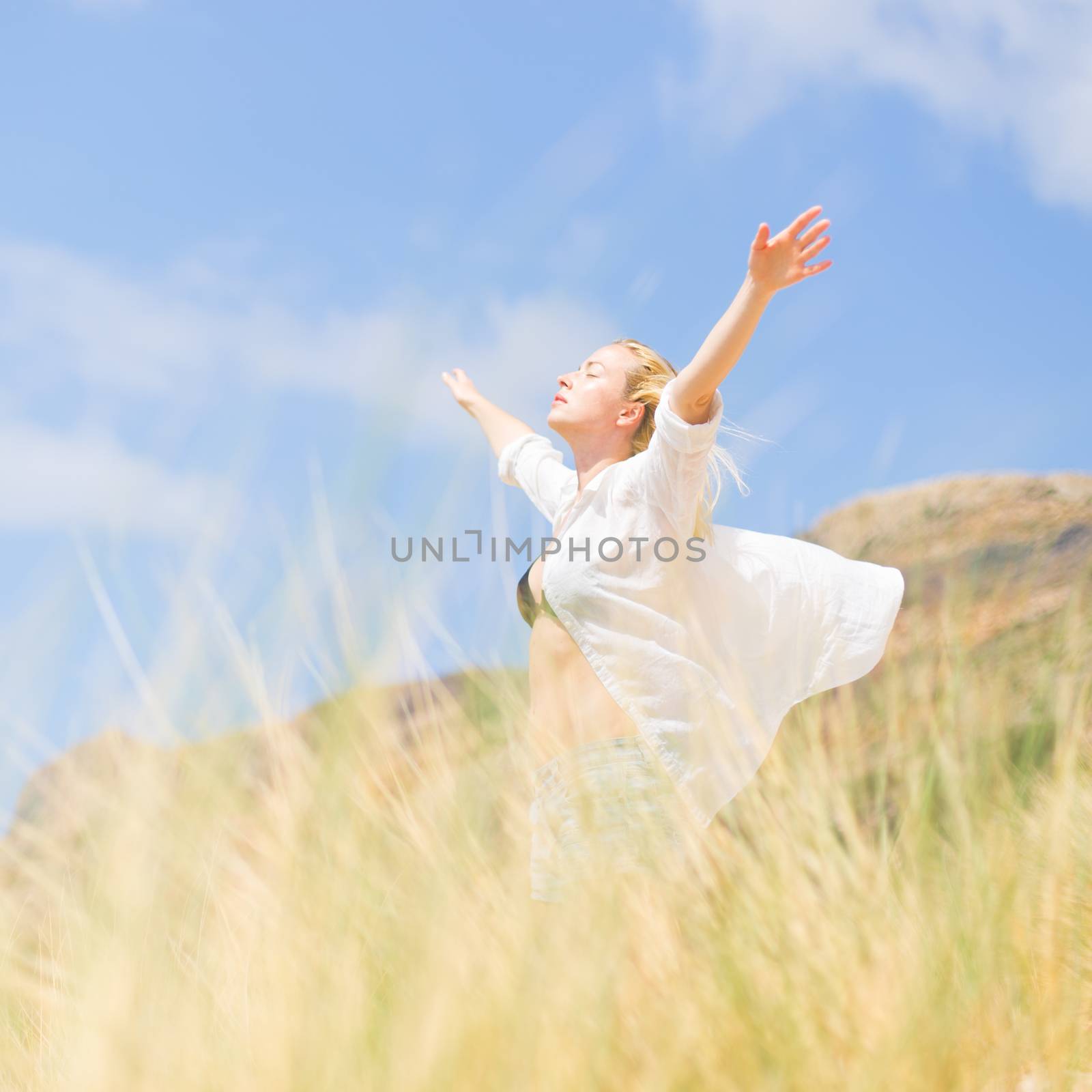 Relaxed woman, arms raised, enjoying sun, freedom and life an a beautiful beach. Young lady feeling free, relaxed and happy. Concept of vacations, freedom, happiness, enjoyment and well being.