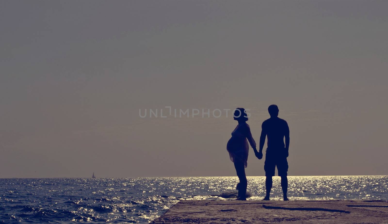 Young Family Waiting for the Miracle.  Romantic Couple on a Beach at Sunset on Background.