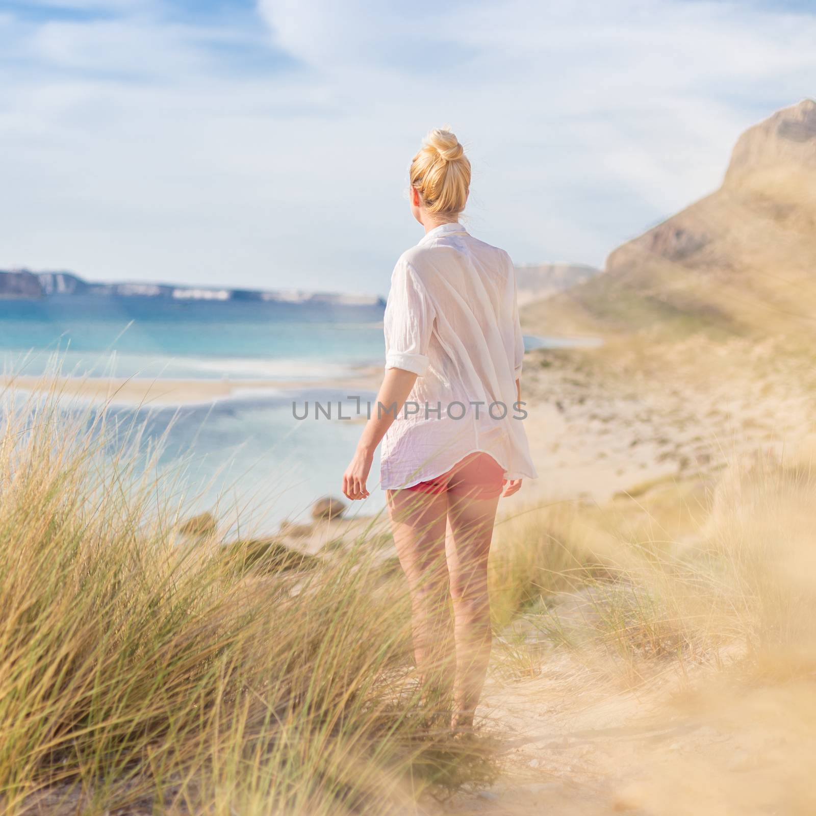 Relaxed woman in white shirt looking at distance, enjoying beautiful nature, freedom and life at serene landscape at Balos beach, Greece. Concept of vacations, freedom, happiness, joy and well being.