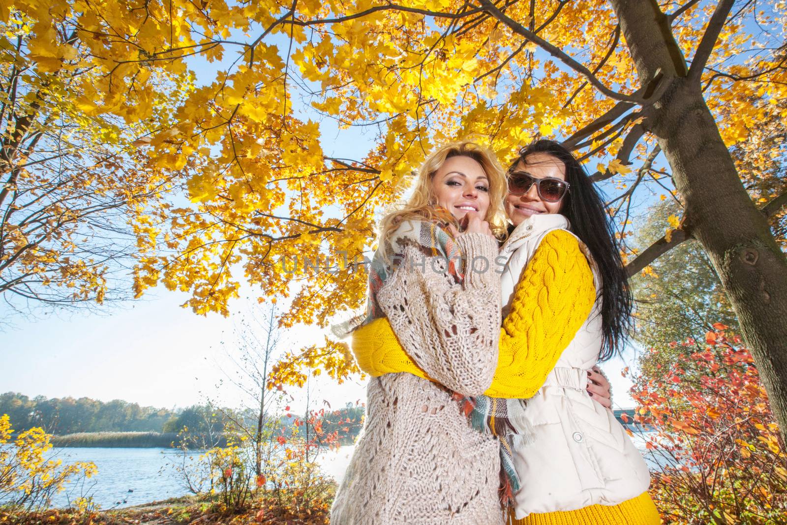 Two cheerful women in autumn park at sunny day