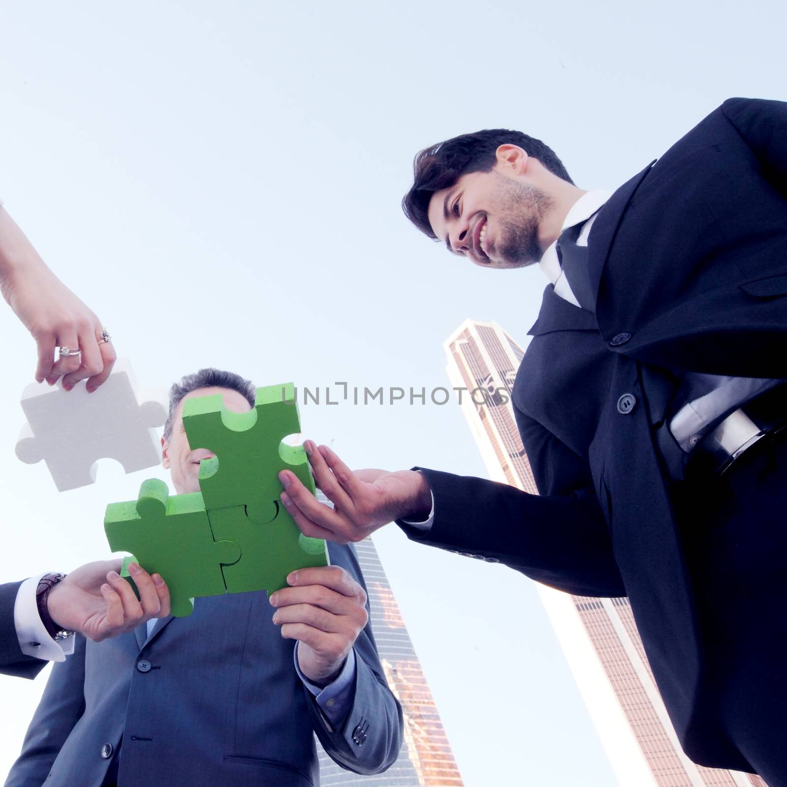 Business people assembling jigsaw puzzle near skyscrapers