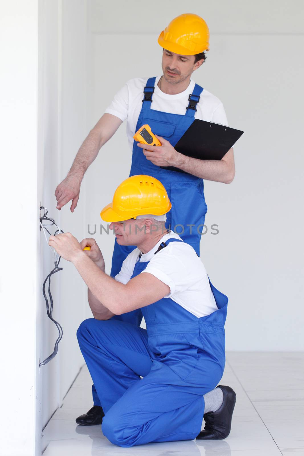 Two builders in helmets working with electricity indoors