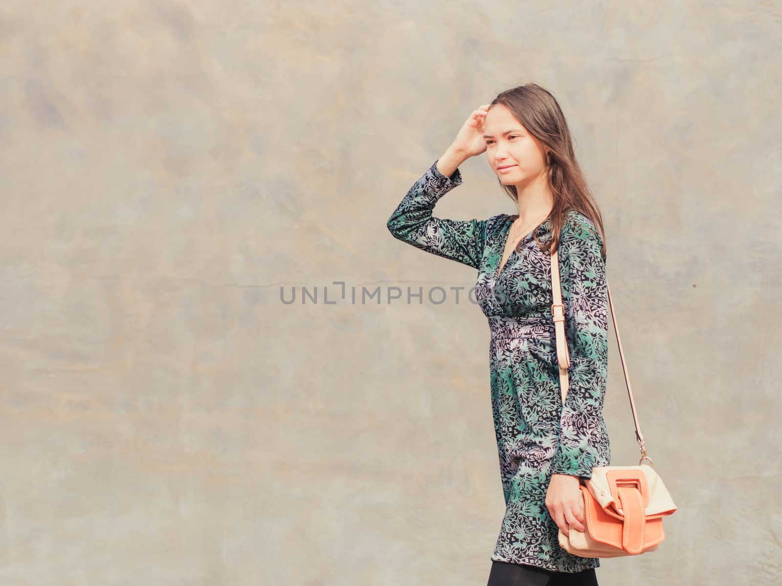 Side view of caucasian woman walking on city street in front of gray wall. Copy space