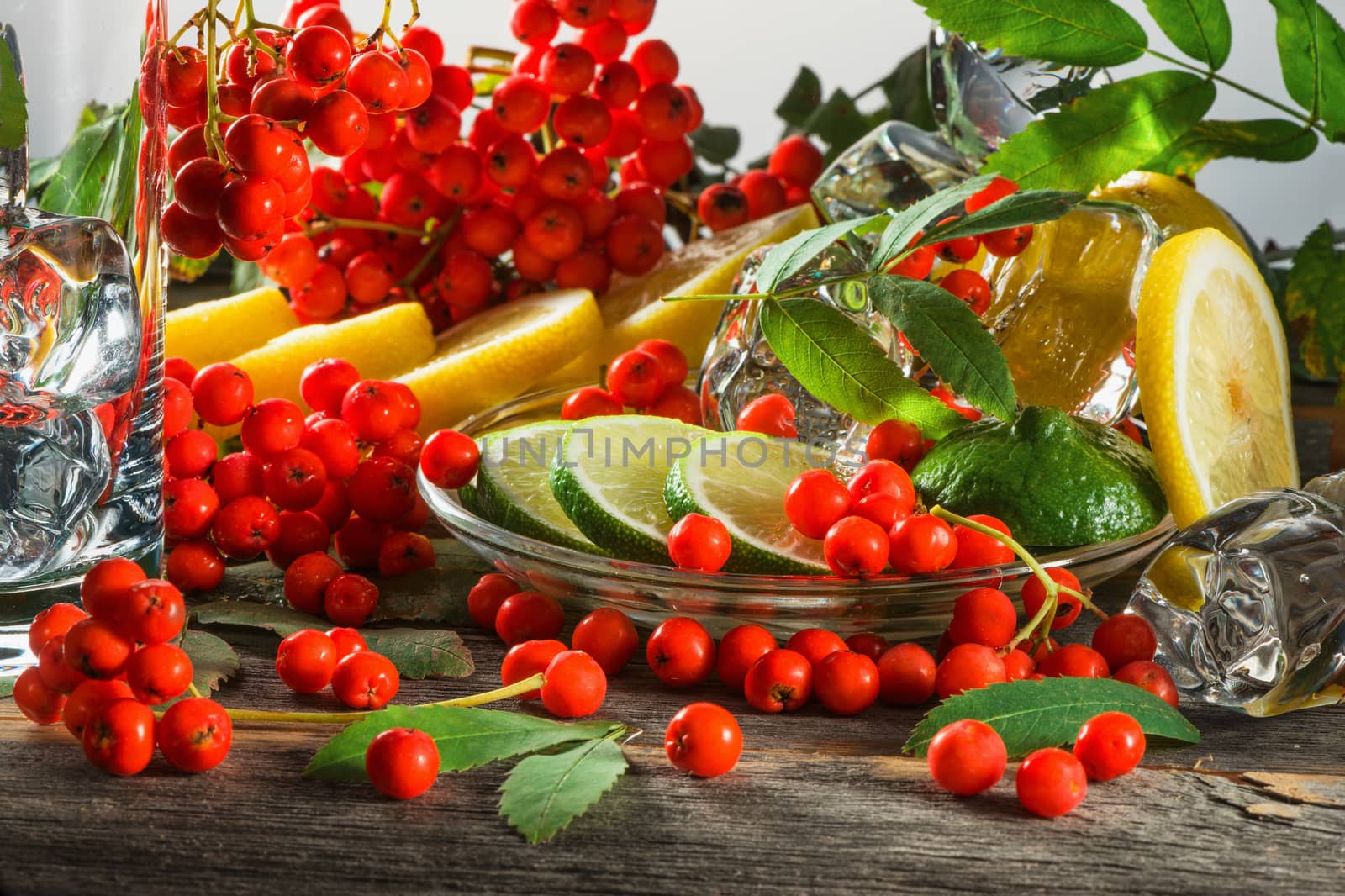 Mountain ash berries on branches with leaves and the cut citrus fruits with ice pieces on a wooden table