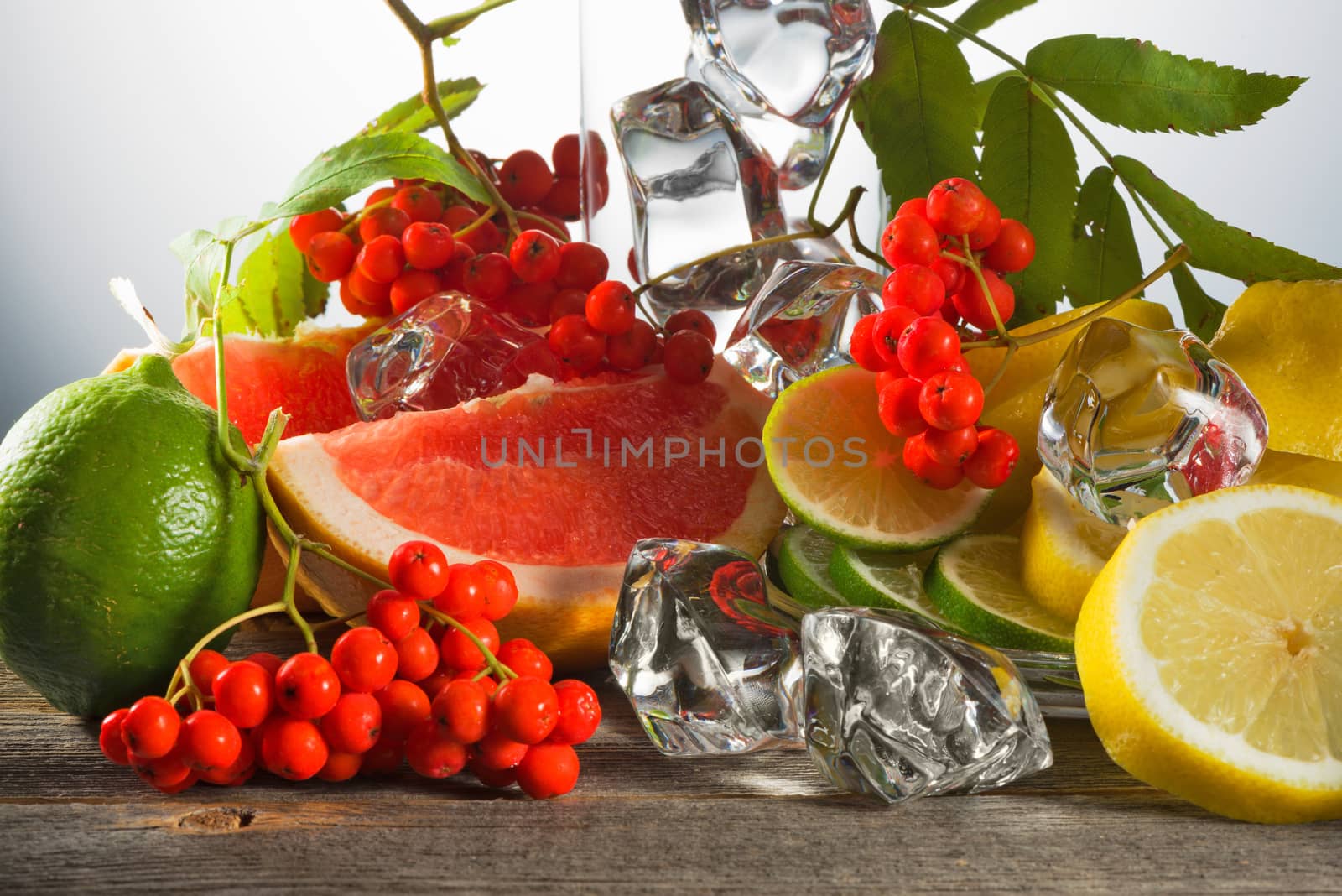 Mountain ash berries on branches with leaves and the cut citrus fruits with ice pieces on wooden boards