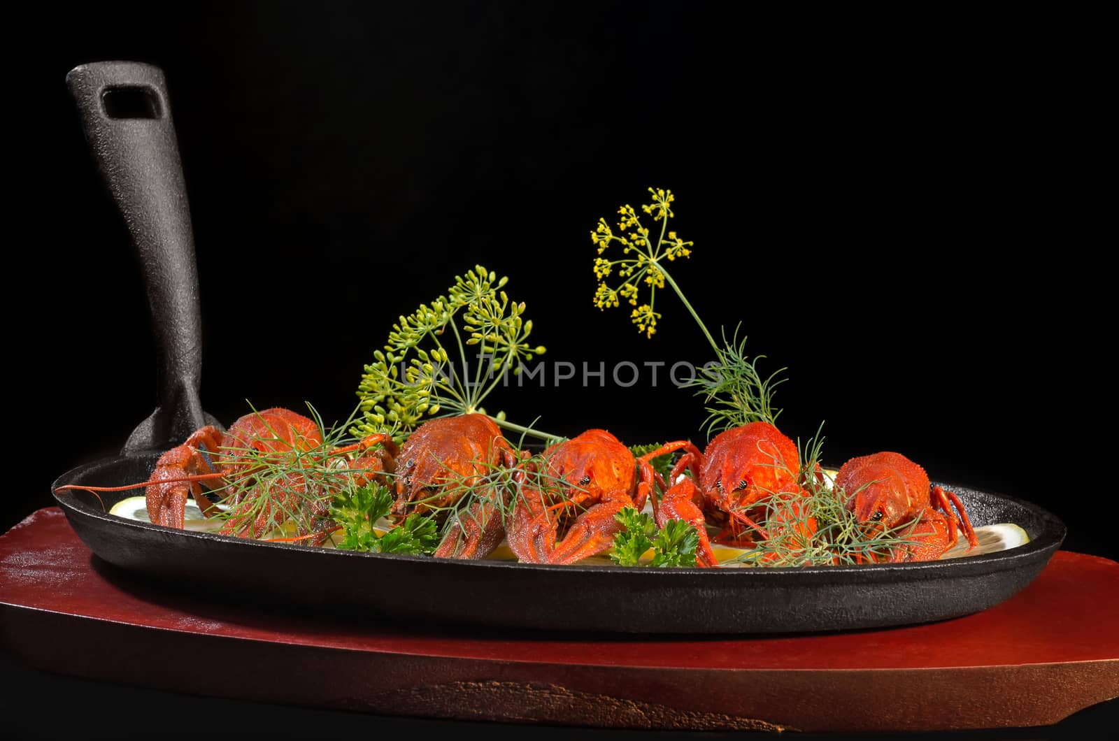 Boiled crawfish with lemon and herbs, in a pan on a wooden stand and a black background