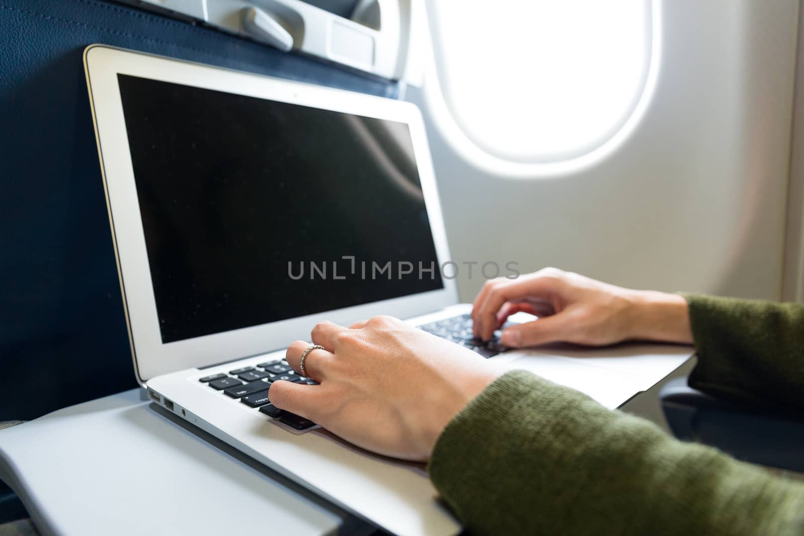 Woman working on laptop computer on board of an airplane by leungchopan